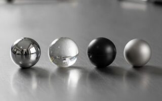 Esferas industriais de diferentes materiais e graus de precisão: aço cromo, vidro, nylon e titânio alinhadas em superfície pl