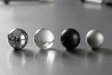 Esferas industriais de diferentes materiais e graus de precisão: aço cromo, vidro, nylon e titânio alinhadas em superfície pl