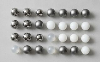 Esferas industriais de diferentes materiais: aço inoxidável, titânio e plástico, dispostas sobre superfície industrial